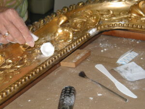A hand applying restoration tools to a metal picture frame